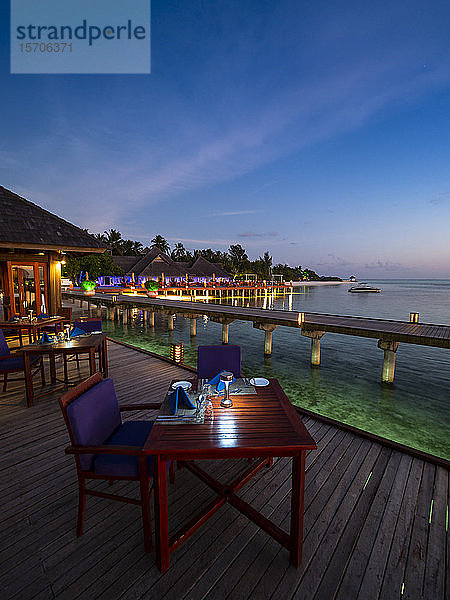 Malediven  Esstische eines Küstenrestaurants in der Abenddämmerung mit Pier im Hintergrund