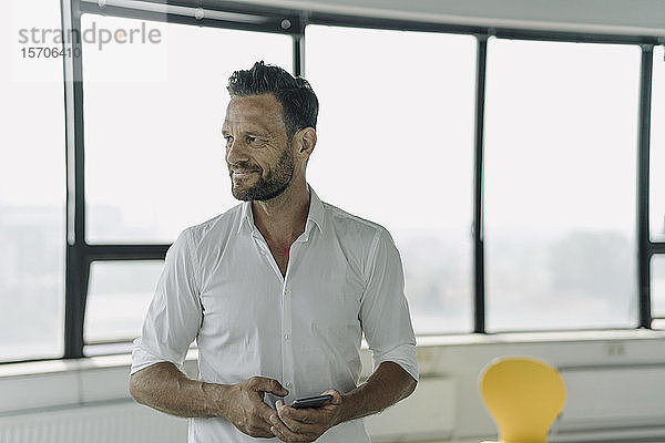 Porträt eines selbstbewussten reifen Geschäftsmannes mit Handy im leeren Büro