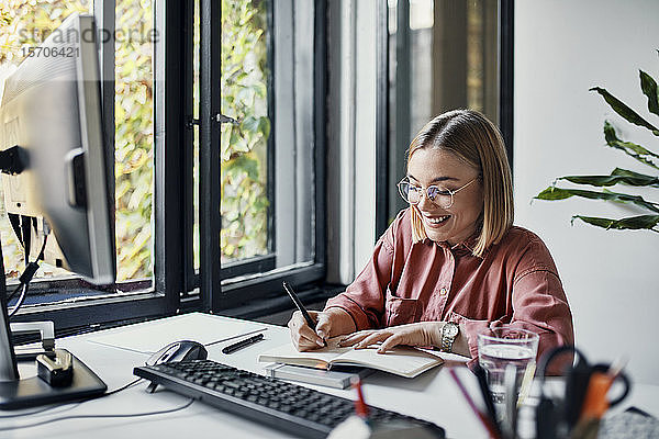 Lächelnde Geschäftsfrau macht Notizen am Schreibtisch im Büro