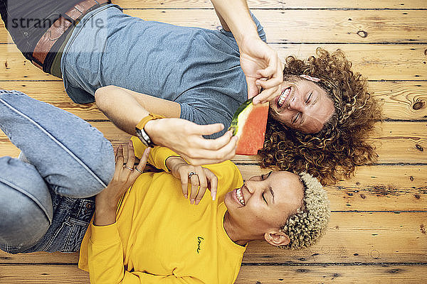 Glückliches junges Paar liegt zu Hause auf dem Boden und teilt sich eine Wassermelone