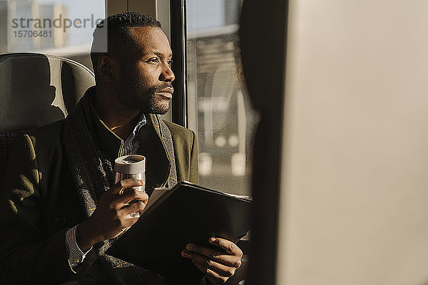 Porträt eines stilvollen Geschäftsmannes mit wiederverwendbarer Tasse und Dokumenten in einem Zug