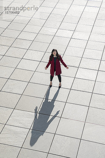 Blick von oben auf eine gehende moderne Geschäftsfrau  die mit offenen Armen auf dem Betonboden steht