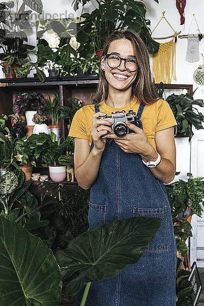 Porträt einer glücklichen jungen Frau mit einer Kamera in einem kleinen Gartenbaubetrieb