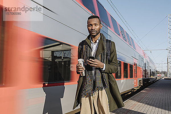 Porträt eines stilvollen Mannes mit Smartphone neben einem Zug