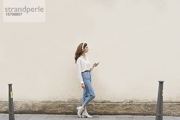 Junge Frau mit Smartphone und Kopfhörern auf dem Bürgersteig