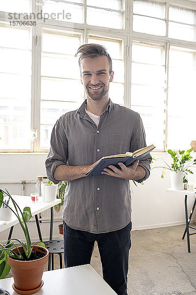 Porträt eines lächelnden Mannes mit Buch in der Hand im Amt