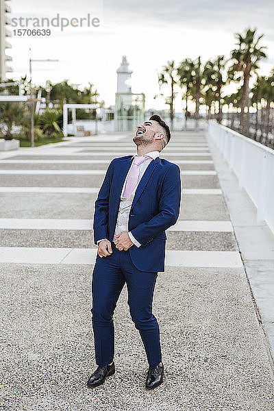 Eleganter Mann steht lachend auf einer Promenade