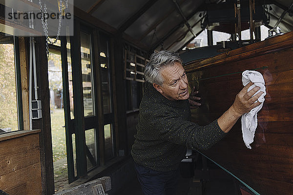 Älterer Mann reinigt Holzboot in einem Bootshaus