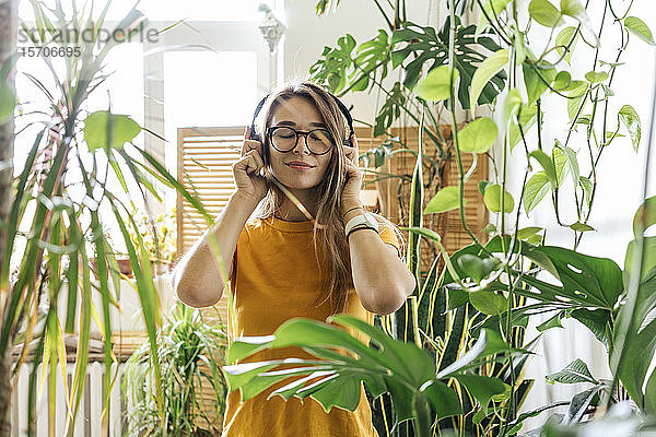 Junge Frau  umgeben von Pflanzen  die mit Kopfhörern Musik hört