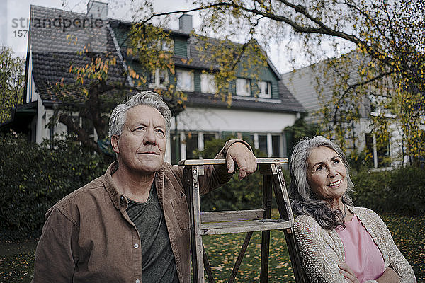 Älteres Ehepaar mit einer Leiter im Garten seines Hauses