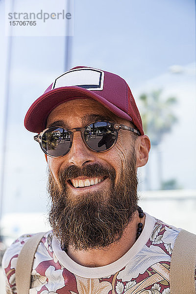 Lächelnder reifer Mann mit Bart  rotem Basecap und Sonnenbrille
