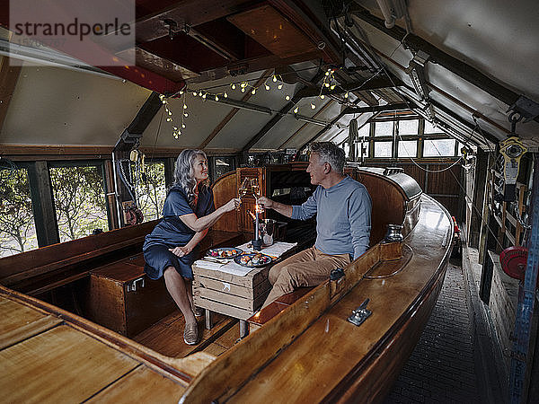 Älteres Ehepaar beim Candle-Light-Dinner auf einem Boot im Bootshaus  Champagnergläser klirrend