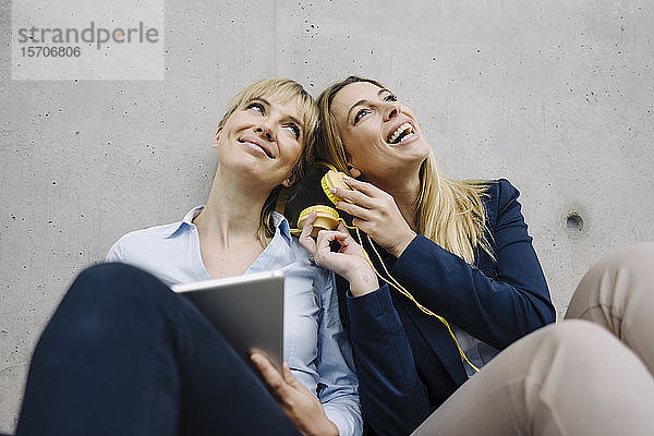 Zwei glückliche junge Geschäftsfrauen teilen sich Kopfhörer