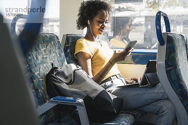 Junge Frau mit Kopfhörern mit Smartphone und Tablet im Zug
