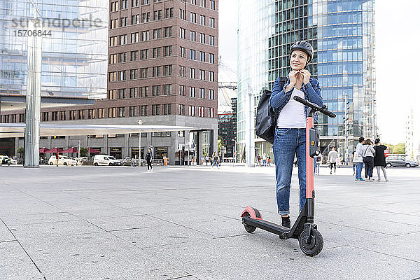 Frau mit E-Scooter in der Stadt  die einen Helm aufsetzt  Berlin  Deutschland