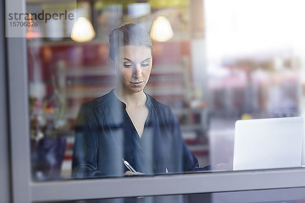 Geschäftsfrau benutzt Laptop hinter einer Fensterscheibe in einem Café