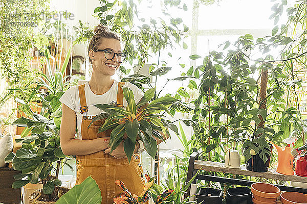 Glückliche junge Frau mit einer Pflanze in einer kleinen Gärtnerei