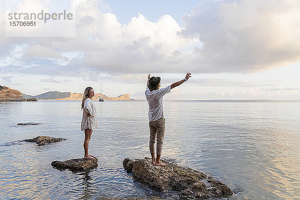 Auf Felsen vor dem Meer stehendes junges Paar  Ibiza  Balearen  Spanien
