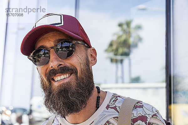 Lächelnder reifer Mann mit Bart  rotem Basecap und Sonnenbrille