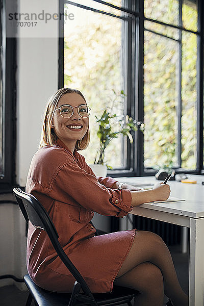 Porträt einer lächelnden Geschäftsfrau  die am Schreibtisch im Büro Notizen macht