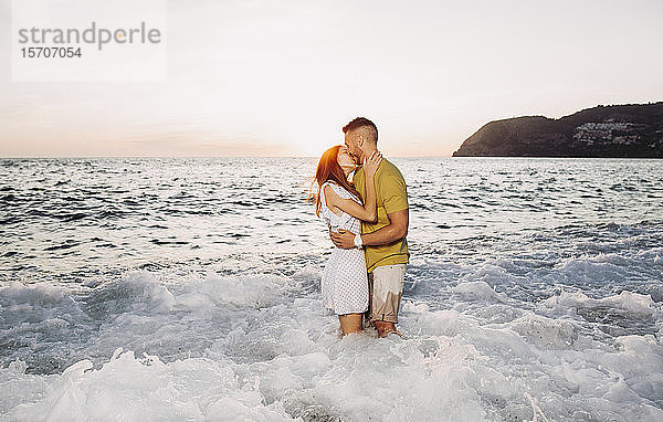 Junges Paar küsst sich bei Sonnenuntergang am Strand
