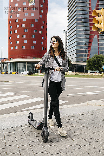 Junge Geschäftsfrau geht mit einem E-Scooter in der Stadt