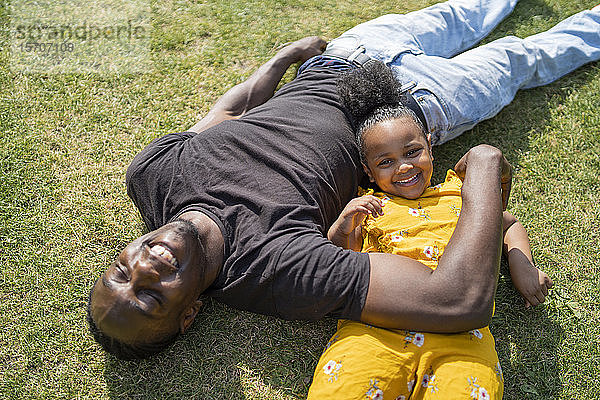 Glückliche Vater und Tochter liegen auf einer Wiese in einem Park