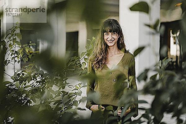 Porträt einer lächelnden brünetten Frau hinter Pflanzen