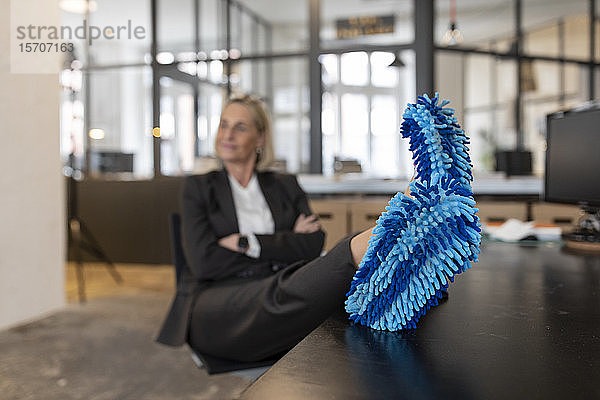 Reife Geschäftsfrau mit Füßen auf dem Schreibtisch  die im Büro Reinigungsschuhe trägt
