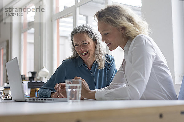 Zwei glückliche Geschäftsfrauen benutzen gemeinsam einen Laptop am Schreibtisch im Büro
