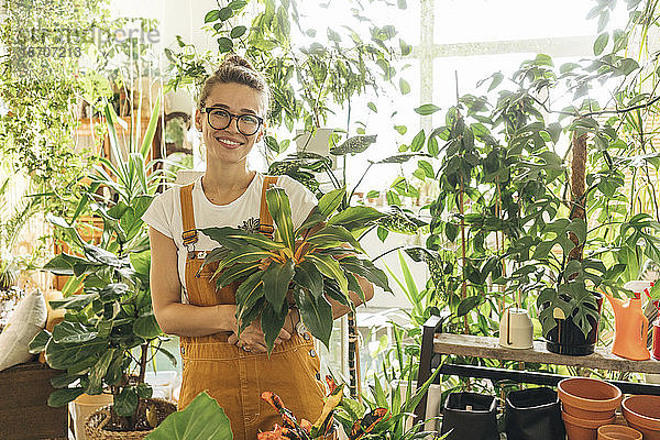 Porträt einer lächelnden jungen Frau  die in einem kleinen Gartengeschäft eine Pflanze hält