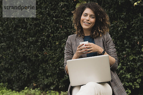 Porträt einer lächelnden Frau mit Kaffee und Laptop im Freien