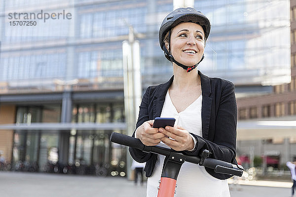 Glückliche Frau mit E-Scooter und Smartphone in der Stadt  Berlin  Deutschland