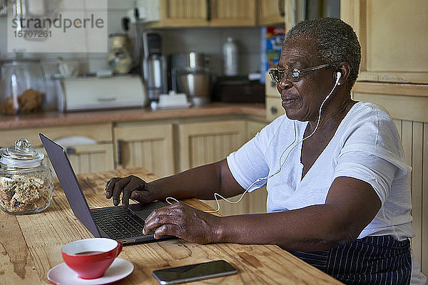 Ältere Frau sitzt mit Laptop am Küchentisch