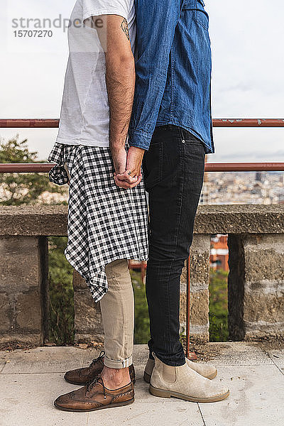 Schrägansicht eines schwulen Paares  das Rücken an Rücken steht und sich an den Händen hält  Barcelona  Spanien