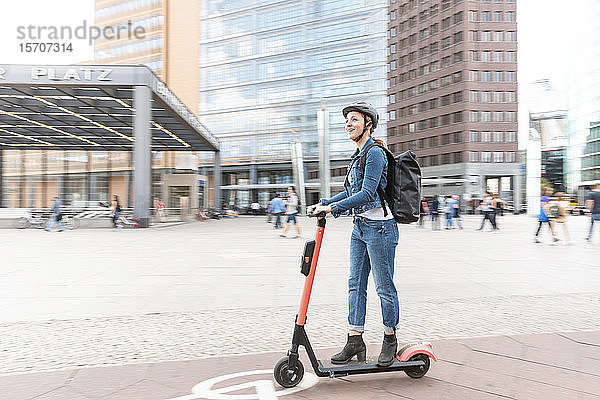 Glückliche Frau fährt E-Scooter in der Stadt  Berlin  Deutschland  Berlin  Deutschland