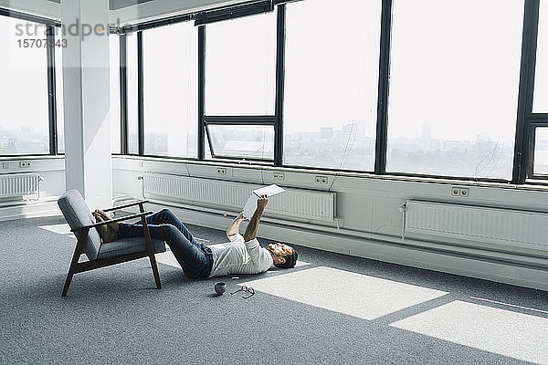 Ein reifer Geschäftsmann  der in einem leeren Büro auf dem Boden liegt und einen Laptop benutzt