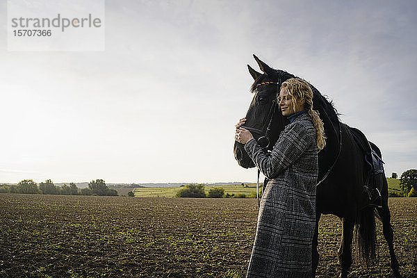 Liebevolle junge Frau mit Pferd auf einem Feld auf dem Land