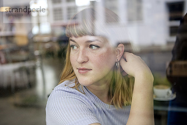 Porträt einer jungen Frau in einem Cafe  die aus dem Fenster schaut