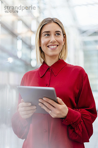Lächelnde junge Geschäftsfrau im roten Hemd mit Tablette