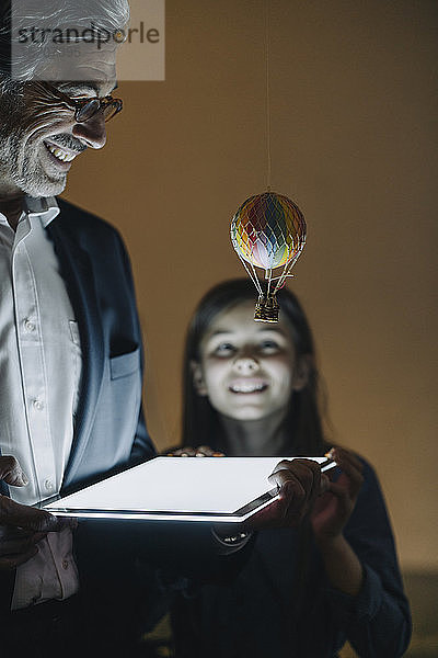 Glücklicher leitender Geschäftsmann und Mädchen mit Heißluftballon und Glanztablette im Büro