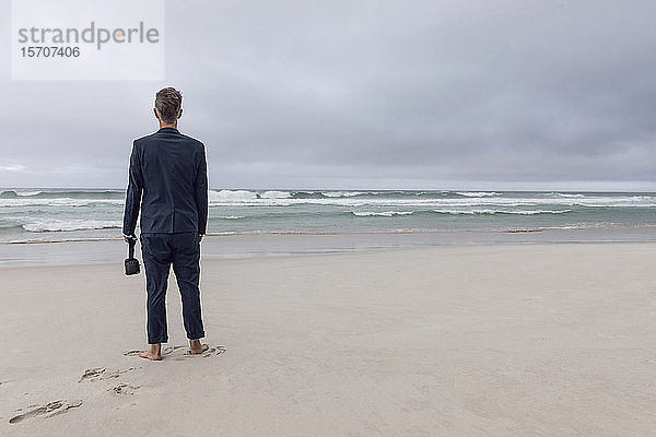 Rückenansicht eines am Strand stehenden Geschäftsmannes mit VR-Brille  Nordhoek  Western Cape  Südafrika