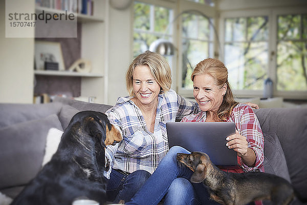 Zwei glückliche reife Frauen mit Hund und Laptop zu Hause