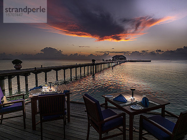 Malediven  Esstische eines Küstenrestaurants in der Abenddämmerung mit Pier im Hintergrund