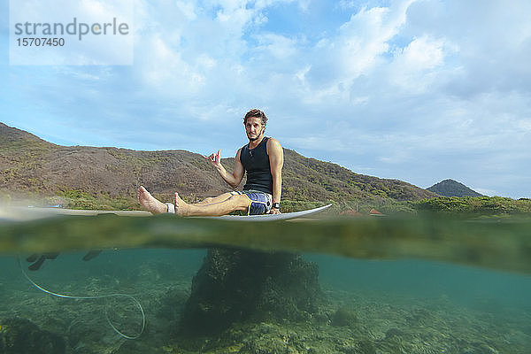 Surfer sitzt auf einem Surfbrett und macht ein Hornschild  Insel Sumbawa  Indonesien