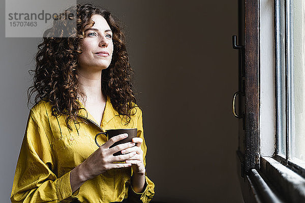 Frau schaut mit Kaffeetasse aus dem Fenster