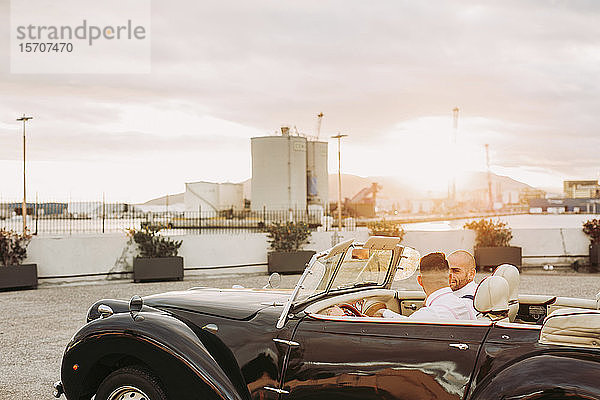 Elegantes schwules Paar in einem Oldtimer-Cabriolet bei Sonnenuntergang