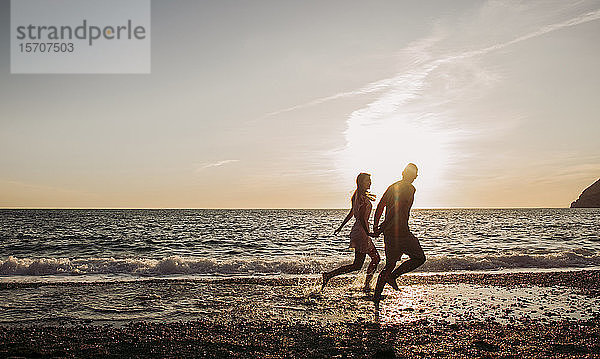 Junges Paar rennt bei Sonnenuntergang am Strand