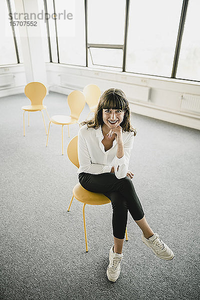 Lächelnde Geschäftsfrau sitzt auf einem Stuhl in einem leeren Büro