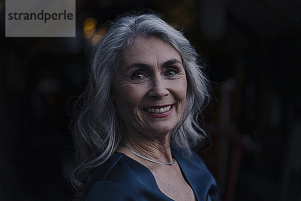 Porträt einer lächelnden reifen Frau im Freien bei Nacht